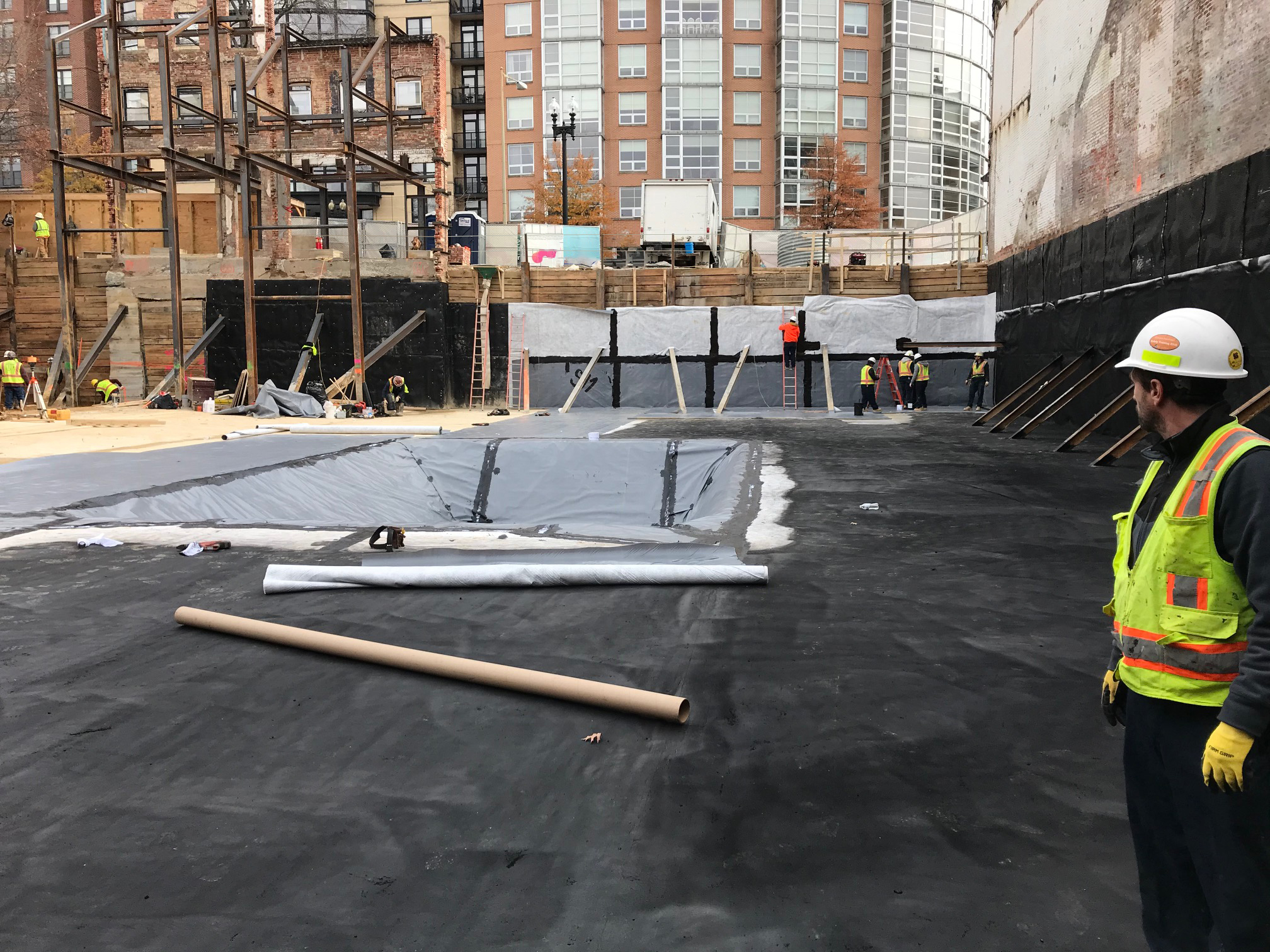 workers applying waterproof material to the ground as part of a construction project.