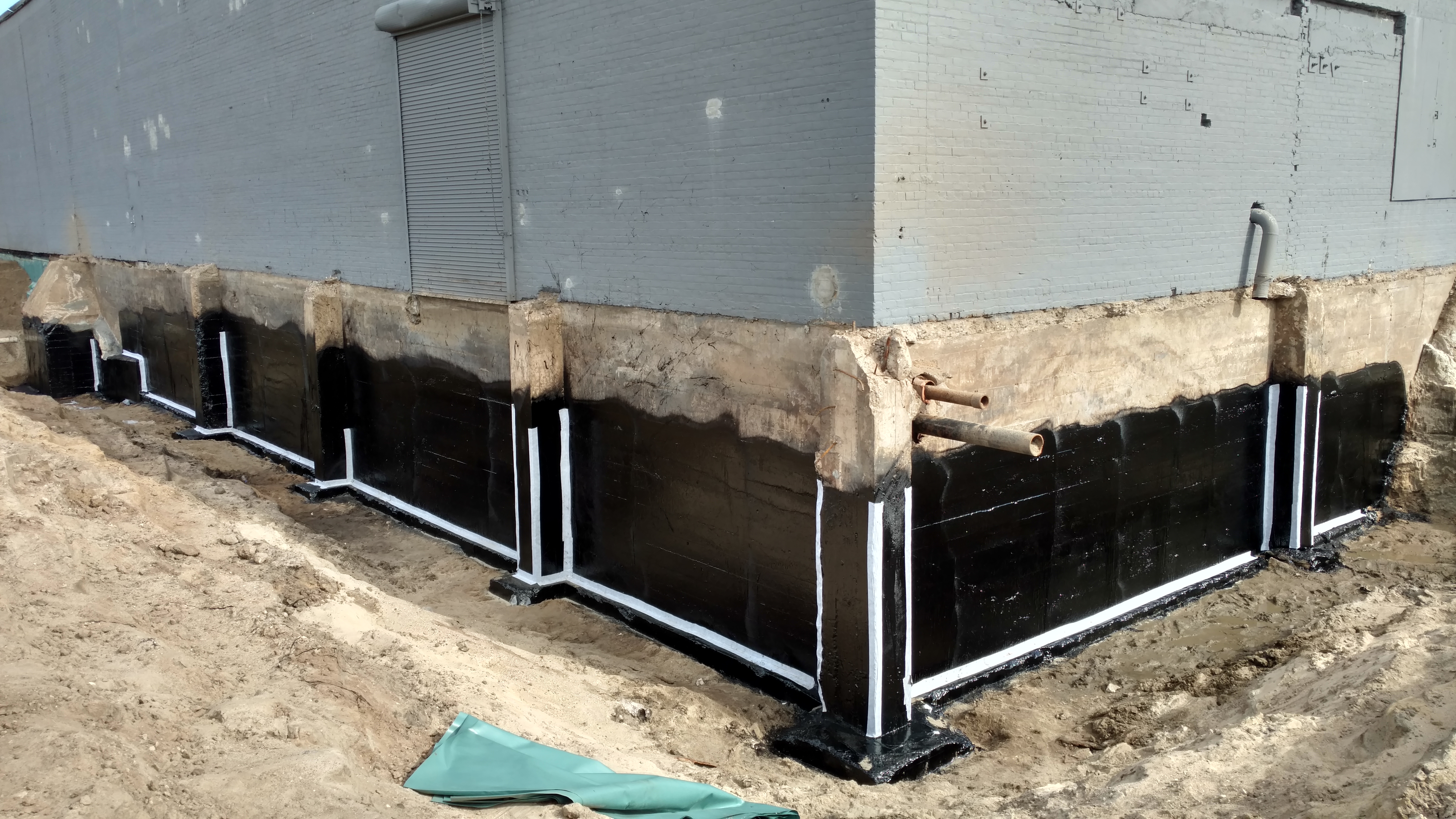the corner of a building under construction, with waterproof foundation applied to the base all around.